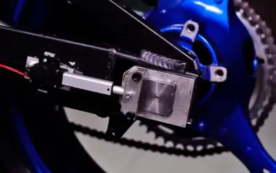 Mecanismo de ajuste para cadena destensada moto, con actuador lineal y soporte metálico sobre basculante azul.
