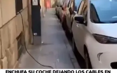 Un coche eléctrico en carga, con cables cruzando la acera, obstaculizando el paso.