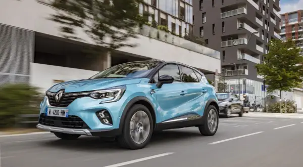 Un coche azul phev Renault Captur circula por una calle urbana moderna, con edificios de cristal y hormigón al fondo.