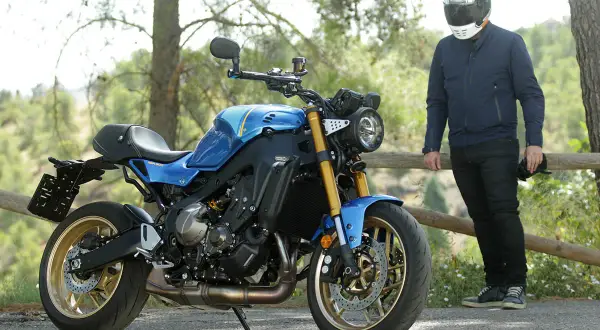 Motocicleta azul de estilo neo retro con detalles dorados, aparcada junto a un hombre con casco.