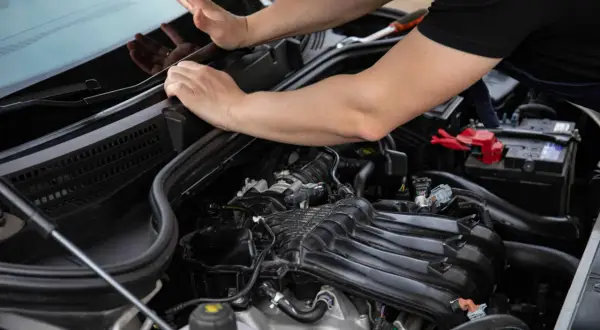 Mecánico revisa el motor de un coche, buscando **problemas PureTech**.