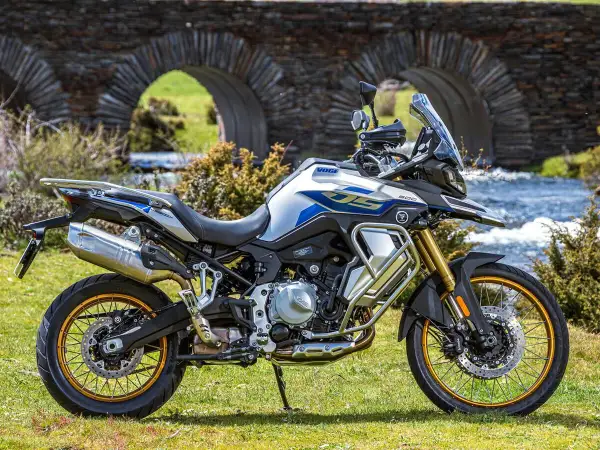 Moto Voge 500DS, una moto china con motor BMW, lista para la aventura junto a un puente de piedra y un río.